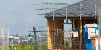 Dočasná stavba: povolení, lhůty a rizika Staveniště s mobilní stavební budkou, na které jsou připnuty papíry se stavebním povolením a harmonogramem, stavbyvedoucí v pozadí drží složku s dokumenty